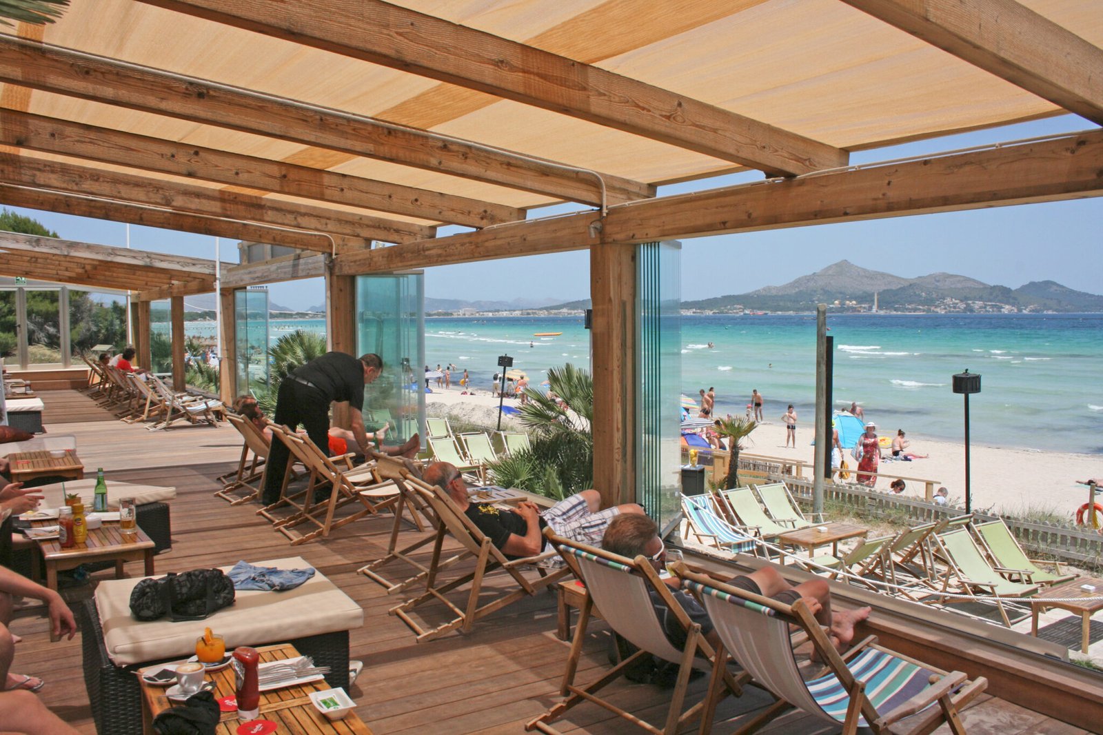 Chiringuito de playa con pérgola de madera y cortinas de cristal sin perfiles con vistas al mar - Cerramiento para hostelería