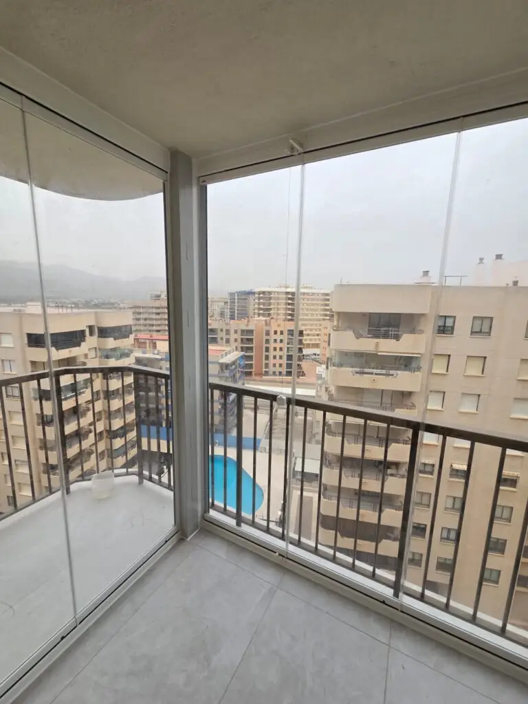 Balcón con cortinas de cristal plegables parcialmente abiertas en Cádiz