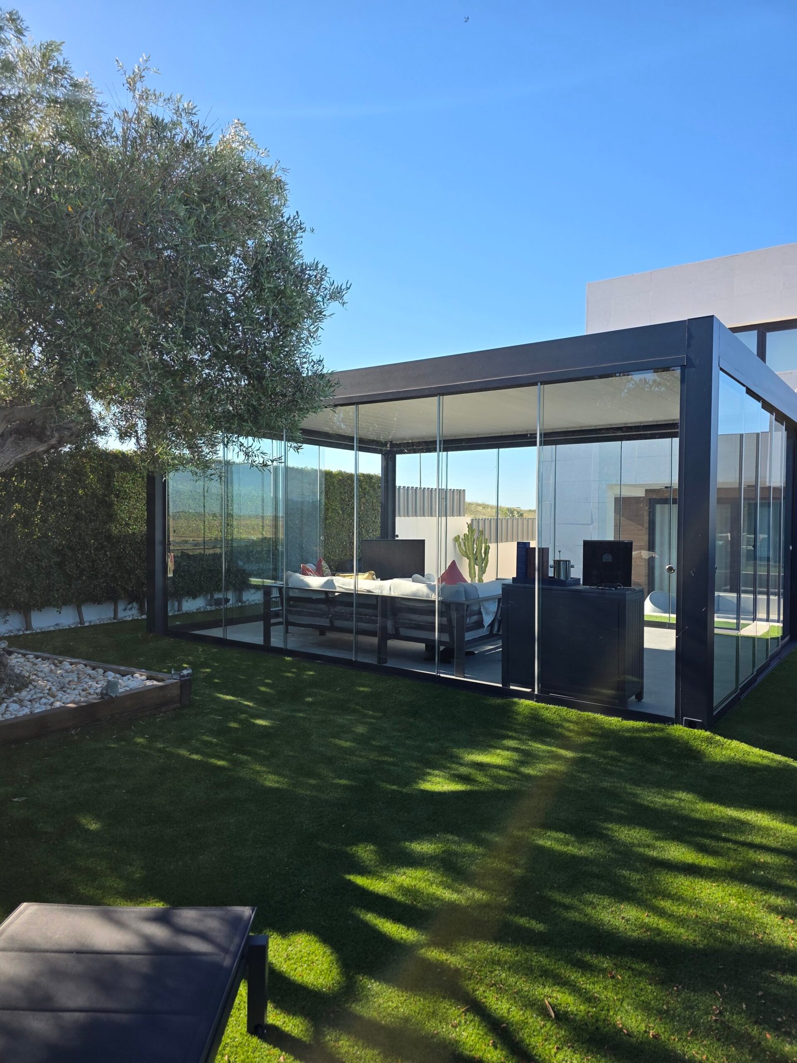 Pérgola bioclimática con correderas de cristal perimetrales en Sanlúcar de Barrameda, vista general del jardín