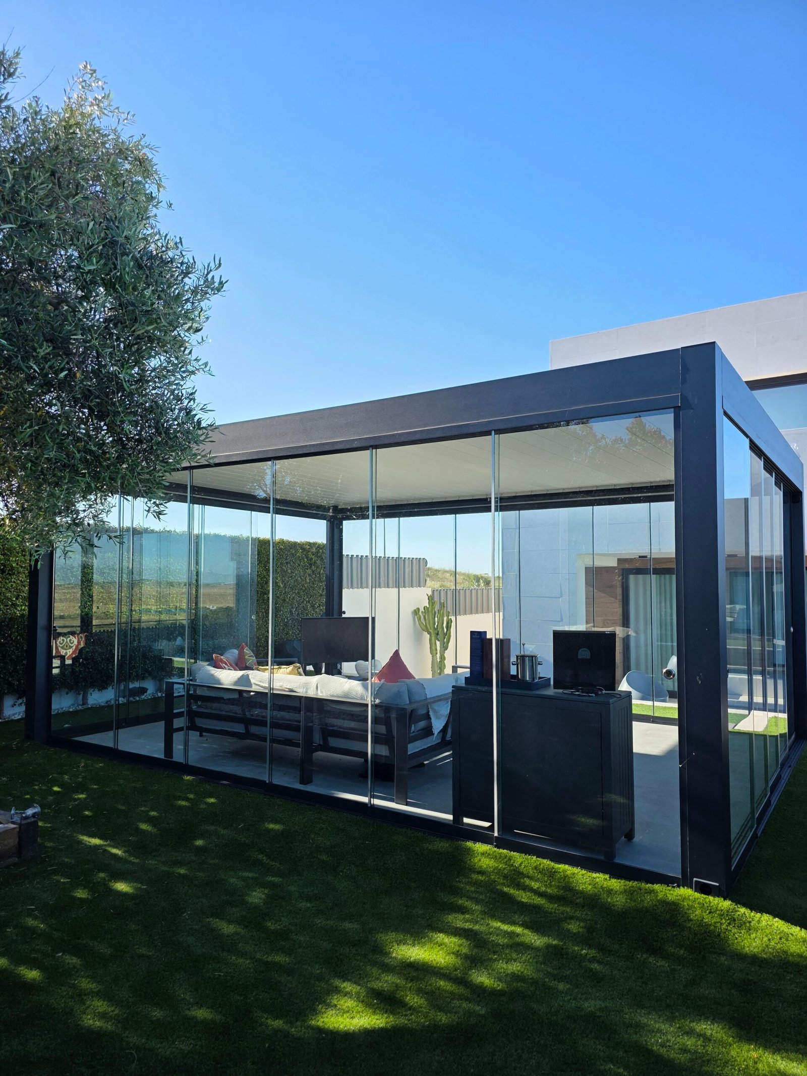 Pérgola bioclimática con correderas perimetrales de cristal en jardín con césped artificial, Sanlúcar de Barrameda
