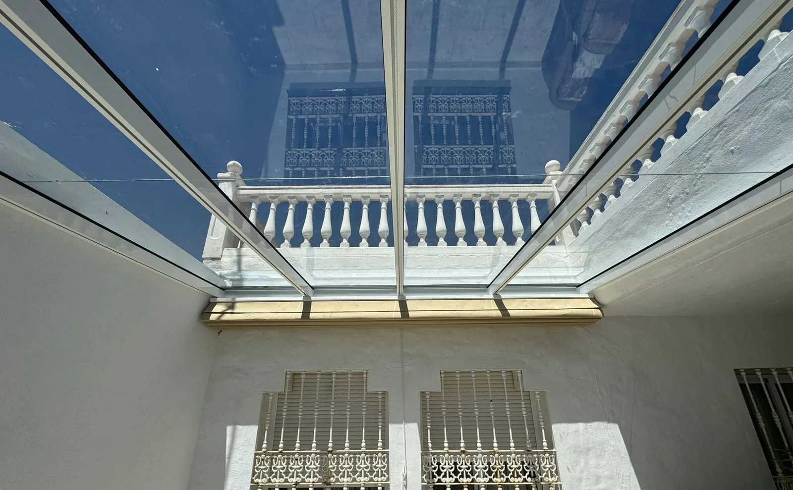 Techo fijo de cristal sobre el patio de una casa tradicional, con balaustrada y rejas de forja