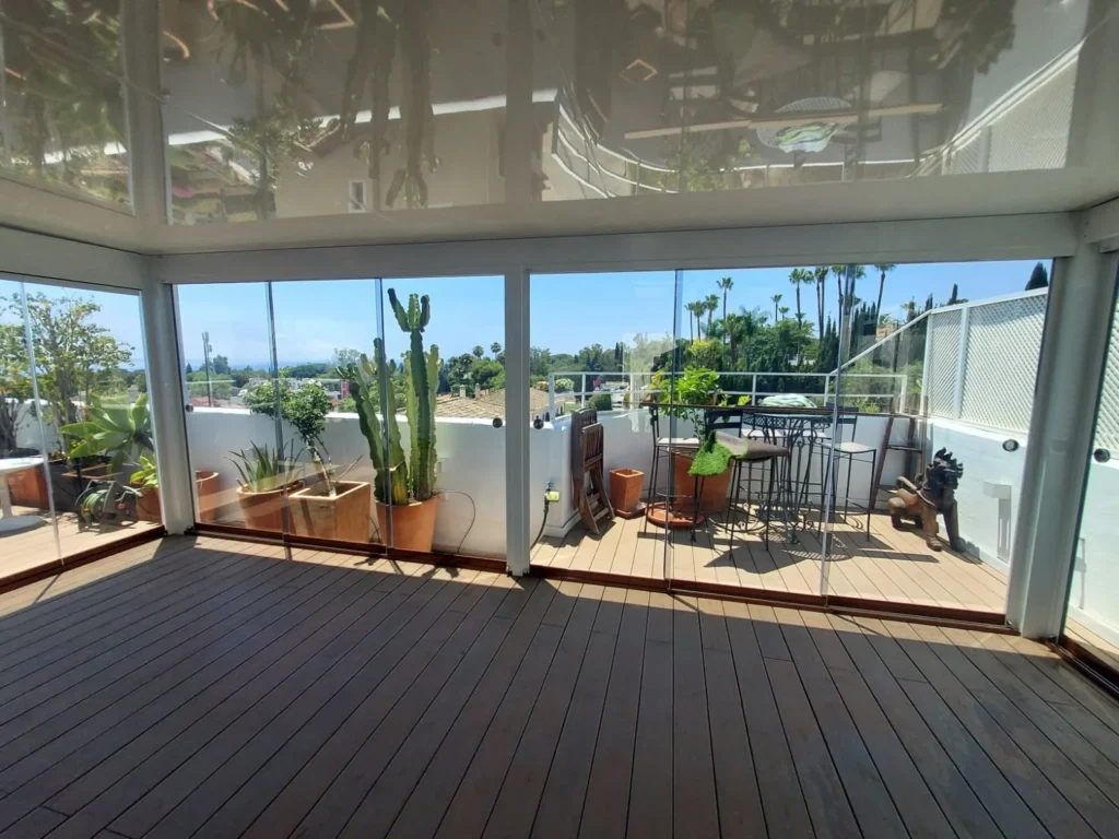 Terraza con suelo de madera cerrada con cortinas de cristal correderas y vistas a jardines