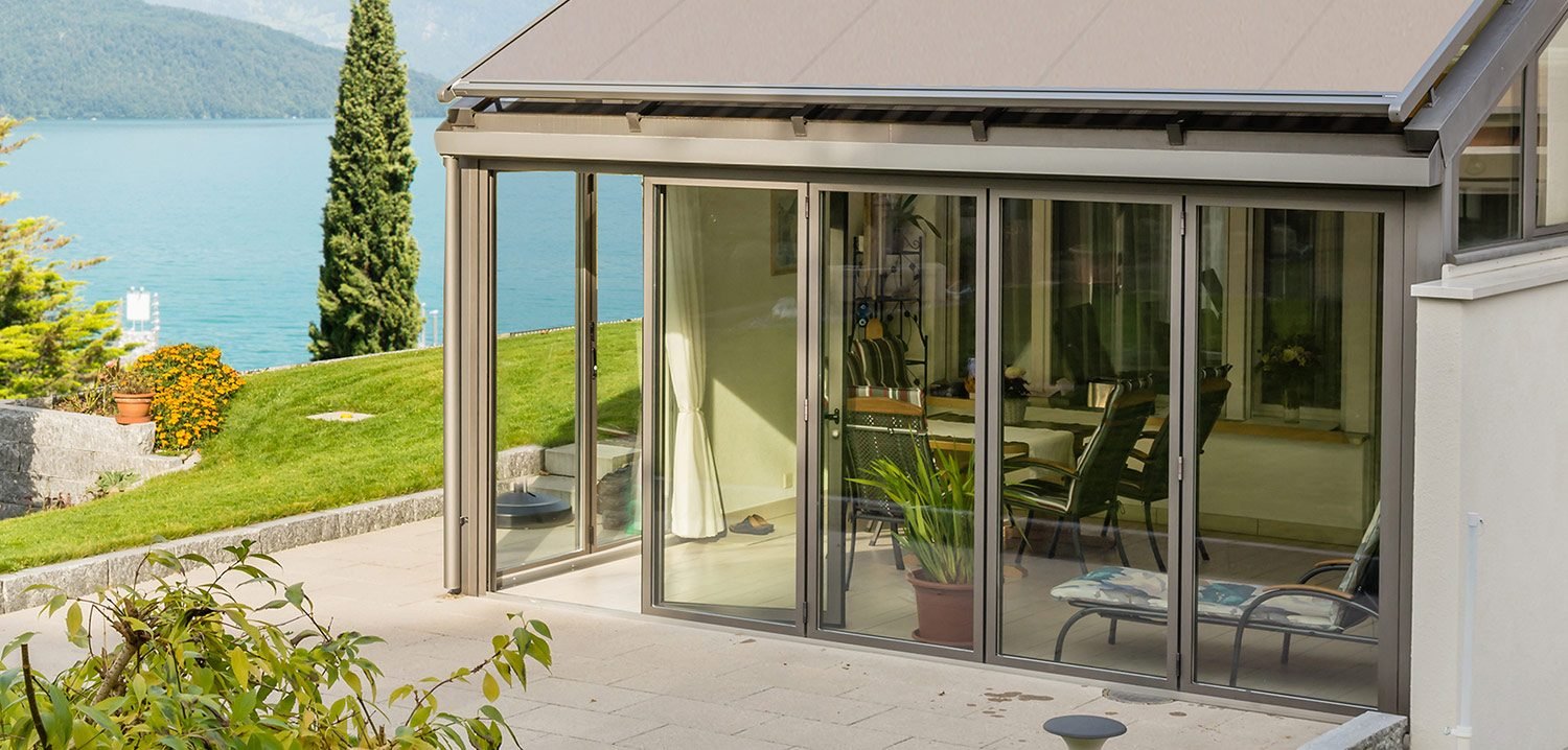 Toldo veranda Habitat SOL extendido sobre el techo de cristal de una terraza cerrada, con vistas al agua
